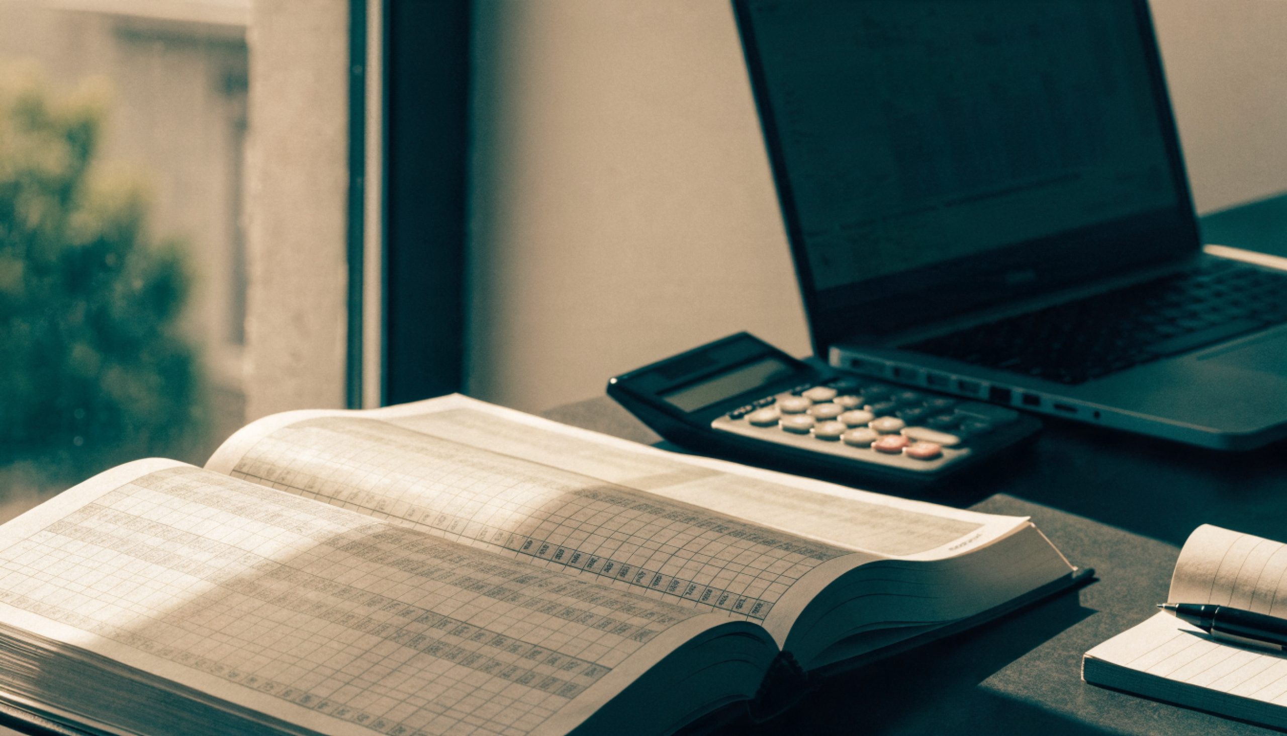 A vehicle value catalogue open on an appraiser desk beside a calculator and a laptop