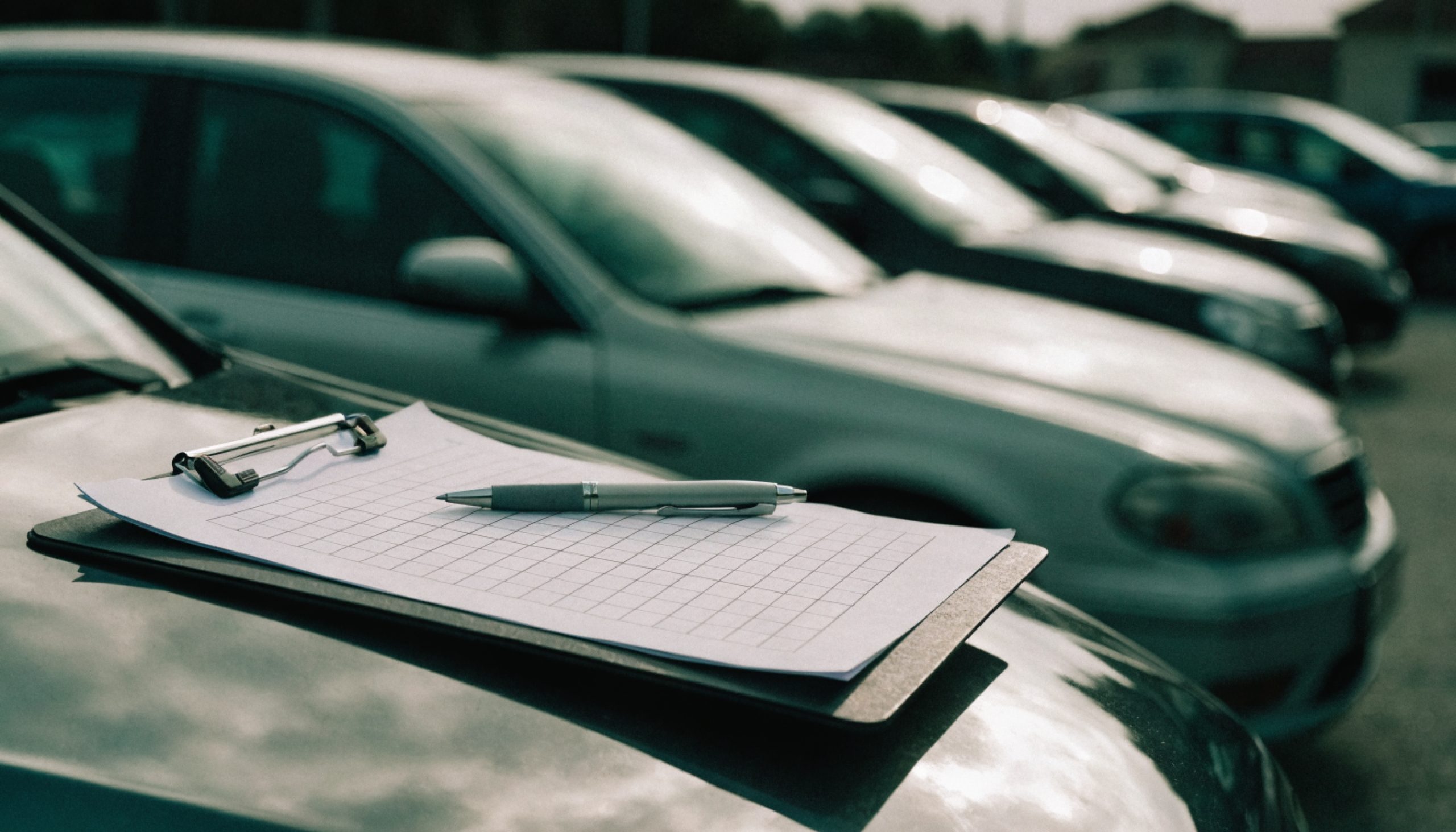 Vehicle valuation table on the bonnet of a car, rows of used cars in the background